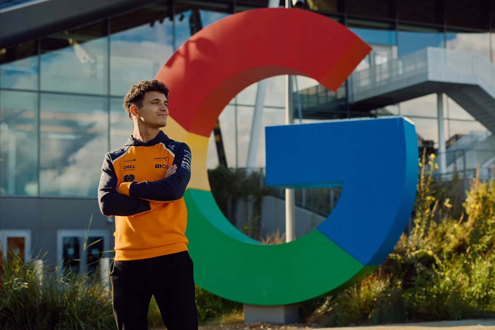 McLaren Racing driver standing in front of a giant Google logo building structure at Google Cloud headquarters.